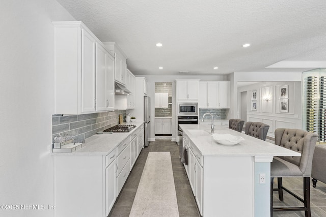 kitchen featuring a kitchen island with sink, stainless steel appliances, light stone countertops, white cabinets, and a kitchen bar