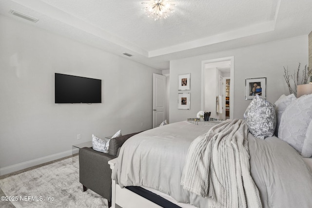 bedroom with a raised ceiling, light carpet, a textured ceiling, and a notable chandelier