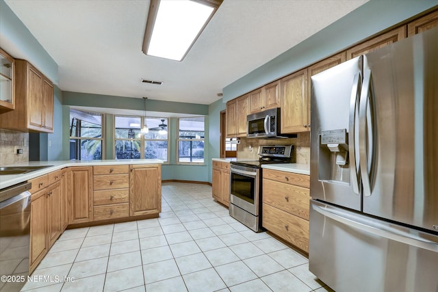 kitchen featuring light tile patterned floors, kitchen peninsula, appliances with stainless steel finishes, decorative backsplash, and decorative light fixtures