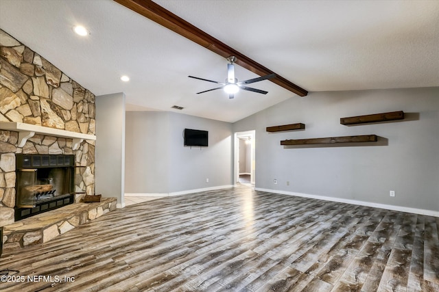 unfurnished living room with ceiling fan, lofted ceiling with beams, wood-type flooring, a stone fireplace, and a textured ceiling