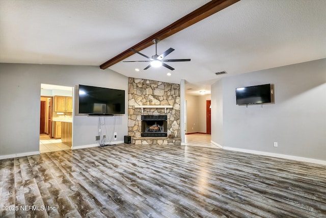 unfurnished living room with a textured ceiling, a stone fireplace, vaulted ceiling with beams, light wood-type flooring, and ceiling fan