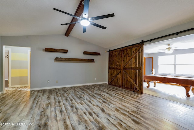 unfurnished living room featuring lofted ceiling with beams, a barn door, light wood-type flooring, and ceiling fan