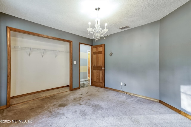 unfurnished bedroom with a closet, an inviting chandelier, a textured ceiling, and carpet flooring