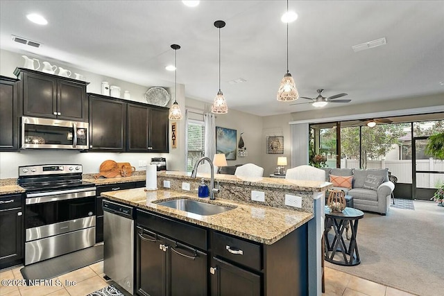 kitchen with pendant lighting, appliances with stainless steel finishes, an island with sink, sink, and light colored carpet