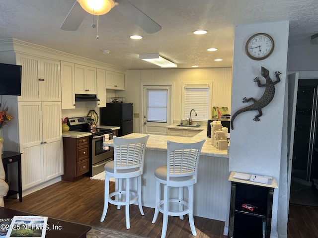 kitchen with sink, dark hardwood / wood-style floors, black fridge, stainless steel range with electric stovetop, and a breakfast bar area