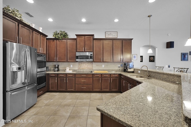 kitchen with kitchen peninsula, appliances with stainless steel finishes, light stone countertops, pendant lighting, and sink