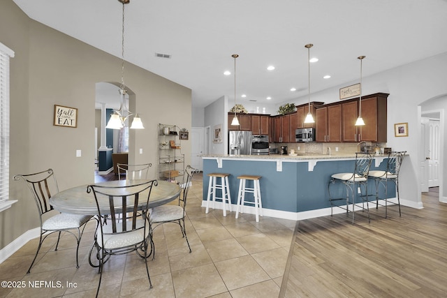 kitchen with decorative light fixtures, stainless steel appliances, backsplash, kitchen peninsula, and light tile patterned floors