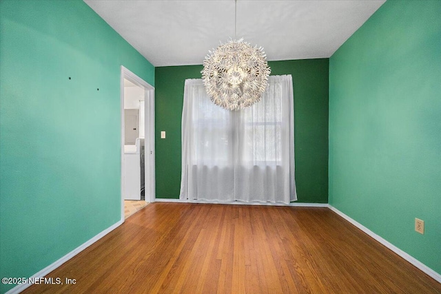 empty room featuring wood-type flooring and an inviting chandelier