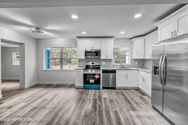 kitchen with appliances with stainless steel finishes, white cabinetry, sink, light wood-type flooring, and a textured ceiling