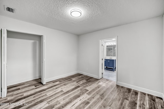 unfurnished bedroom featuring hardwood / wood-style flooring, a closet, ensuite bathroom, and a textured ceiling