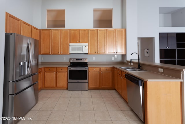 kitchen with a high ceiling, appliances with stainless steel finishes, sink, kitchen peninsula, and light tile patterned flooring