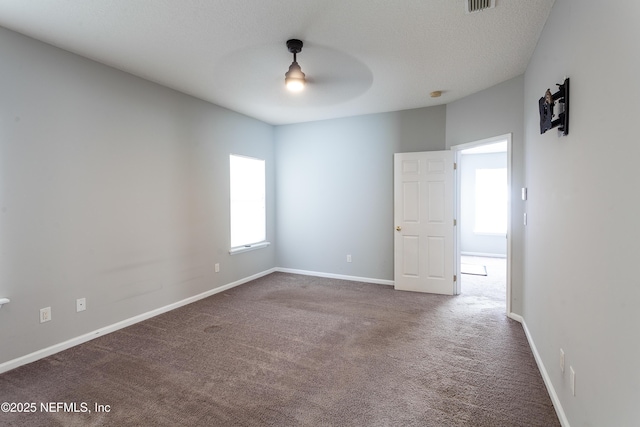 unfurnished room featuring ceiling fan, dark carpet, and a healthy amount of sunlight