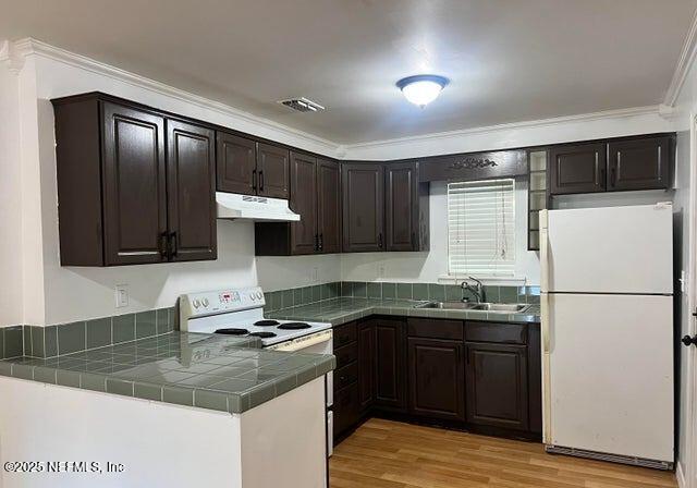 kitchen with white appliances, sink, ornamental molding, kitchen peninsula, and dark brown cabinets