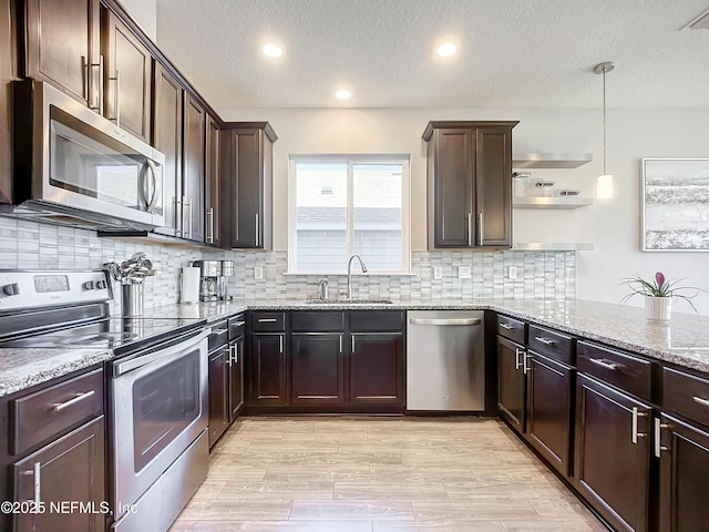 kitchen with pendant lighting, sink, light wood-type flooring, light stone countertops, and stainless steel appliances