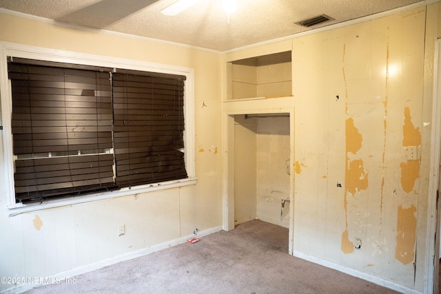 empty room with a textured ceiling, crown molding, and light carpet