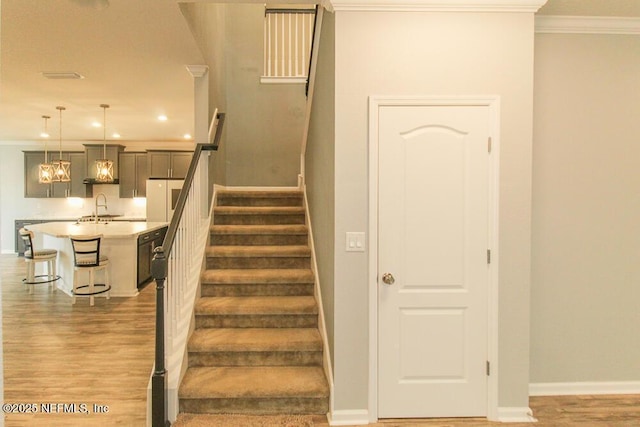 staircase with hardwood / wood-style floors, crown molding, and sink