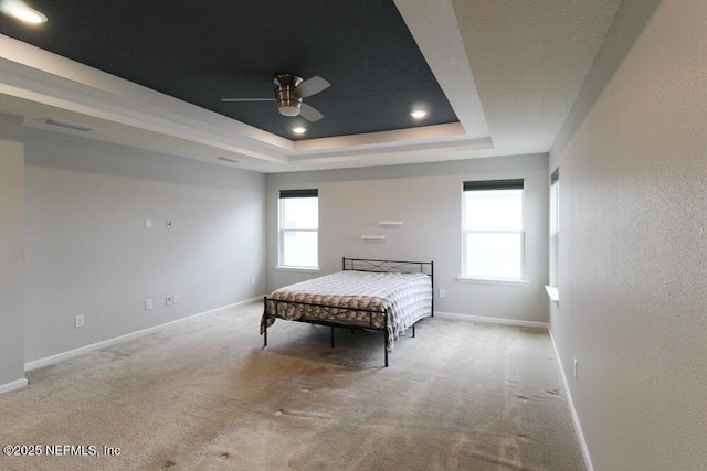 carpeted bedroom featuring ceiling fan, a tray ceiling, and multiple windows