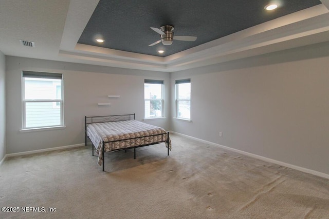 carpeted bedroom featuring ceiling fan and a tray ceiling