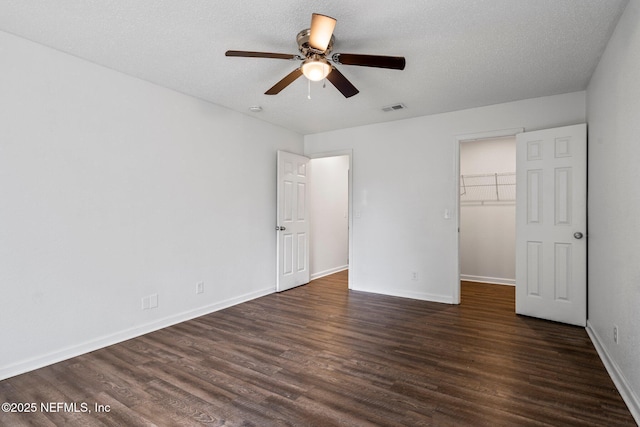 unfurnished bedroom with a spacious closet, ceiling fan, dark hardwood / wood-style floors, a closet, and a textured ceiling