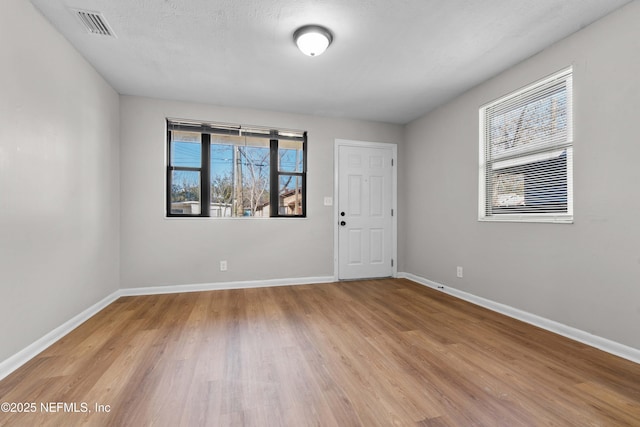 empty room with light wood-type flooring and a textured ceiling