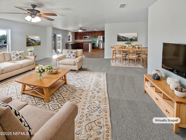 carpeted living room featuring ceiling fan and a textured ceiling