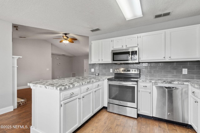 kitchen with tasteful backsplash, kitchen peninsula, white cabinets, and appliances with stainless steel finishes