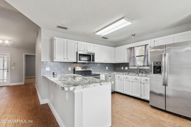 kitchen featuring tasteful backsplash, appliances with stainless steel finishes, kitchen peninsula, light stone countertops, and white cabinets