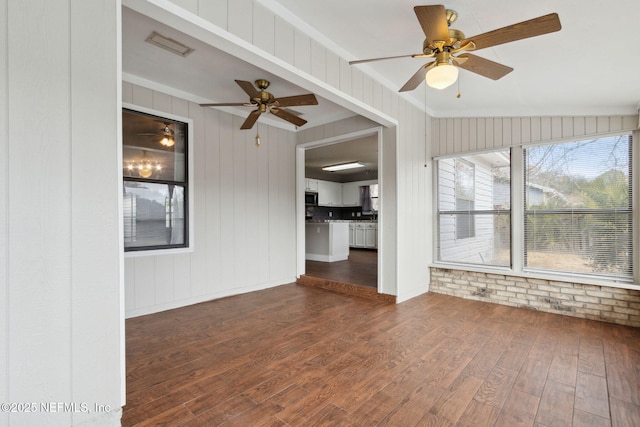 unfurnished living room with dark hardwood / wood-style flooring, ceiling fan, and brick wall