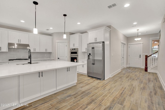 kitchen featuring appliances with stainless steel finishes, white cabinetry, tasteful backsplash, sink, and hanging light fixtures