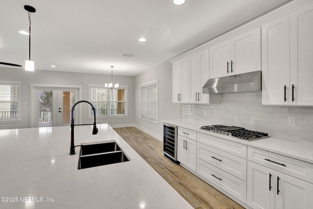 kitchen featuring decorative light fixtures, sink, white cabinetry, light stone countertops, and beverage cooler