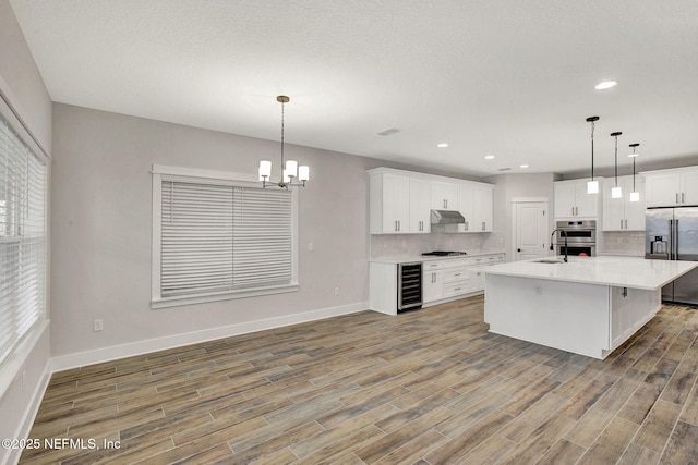 kitchen with an island with sink, white cabinetry, wine cooler, and stainless steel appliances