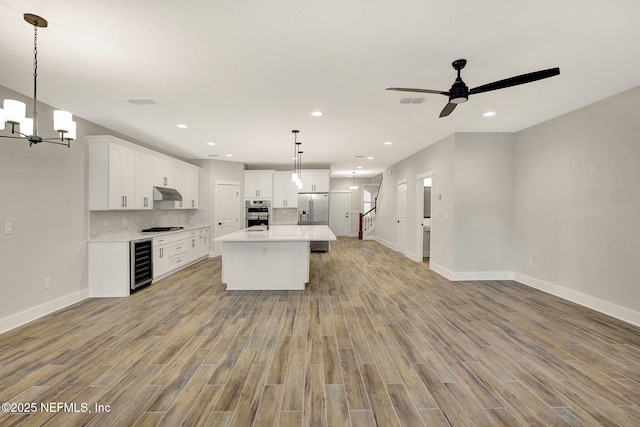 kitchen featuring a kitchen island with sink, white cabinetry, beverage cooler, and appliances with stainless steel finishes