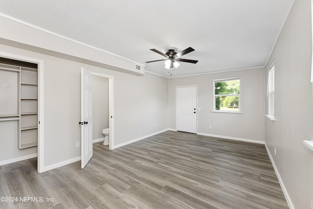 unfurnished bedroom featuring ceiling fan, hardwood / wood-style flooring, ensuite bathroom, and crown molding