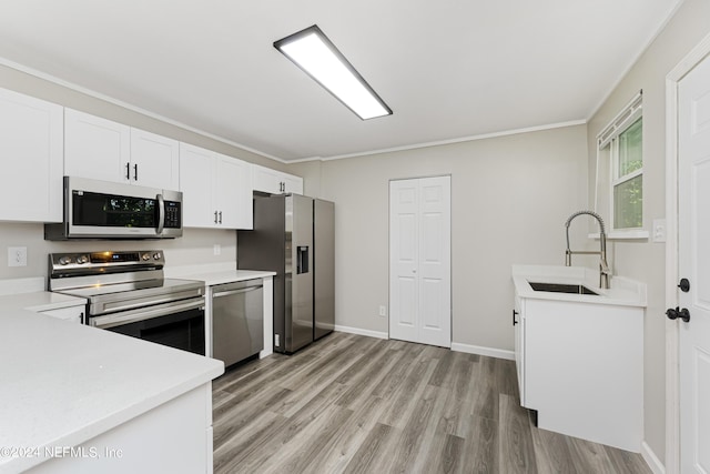 kitchen featuring white cabinetry, light hardwood / wood-style floors, appliances with stainless steel finishes, ornamental molding, and sink