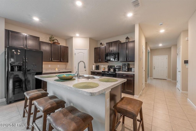 kitchen featuring black appliances, a kitchen bar, sink, a kitchen island with sink, and light tile patterned floors