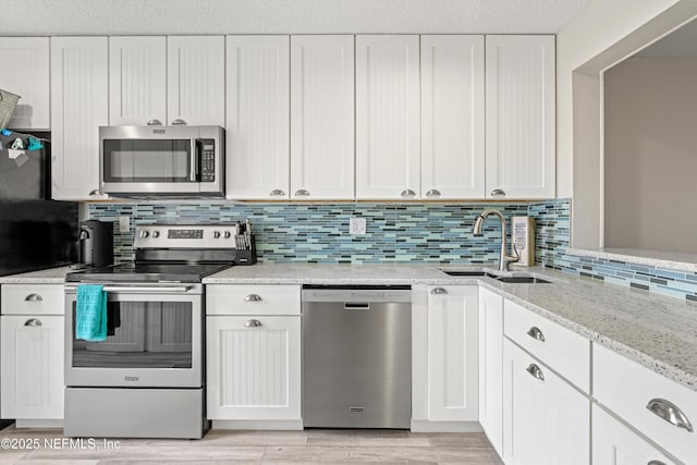 kitchen with tasteful backsplash, white cabinets, sink, and stainless steel appliances