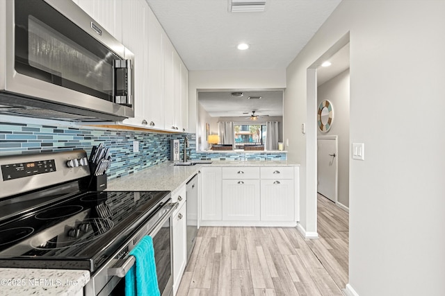 kitchen with ceiling fan, appliances with stainless steel finishes, backsplash, white cabinets, and light hardwood / wood-style flooring