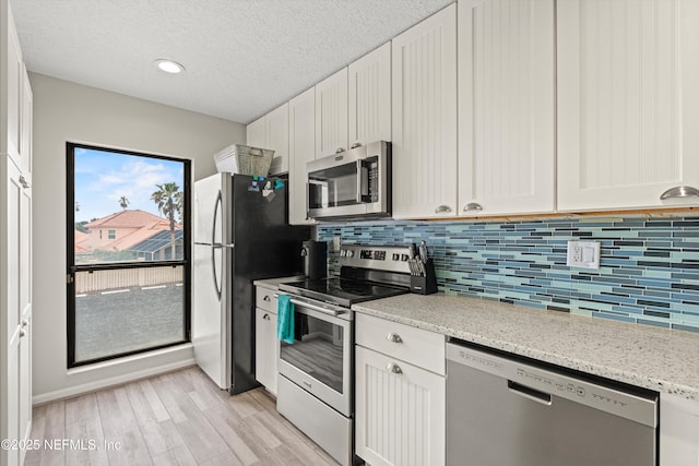 kitchen featuring plenty of natural light, appliances with stainless steel finishes, white cabinets, and light stone countertops