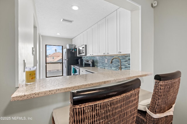 kitchen with decorative backsplash, appliances with stainless steel finishes, a textured ceiling, white cabinets, and light stone counters