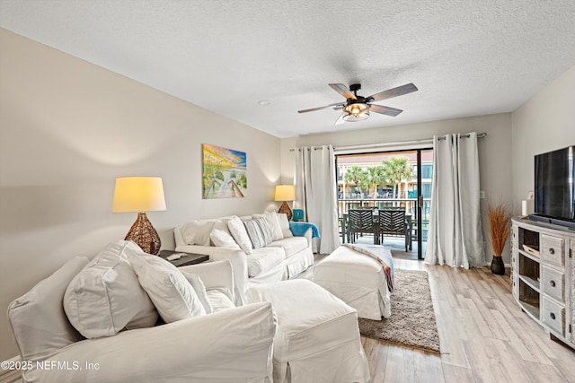 living room with ceiling fan, light wood-type flooring, and a textured ceiling