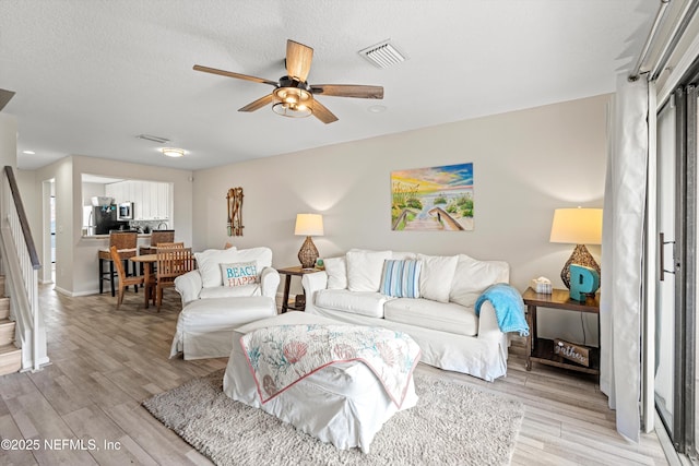 living room with ceiling fan, a textured ceiling, and light hardwood / wood-style flooring