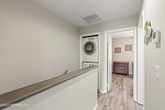 hall with stacked washer / drying machine and light hardwood / wood-style floors