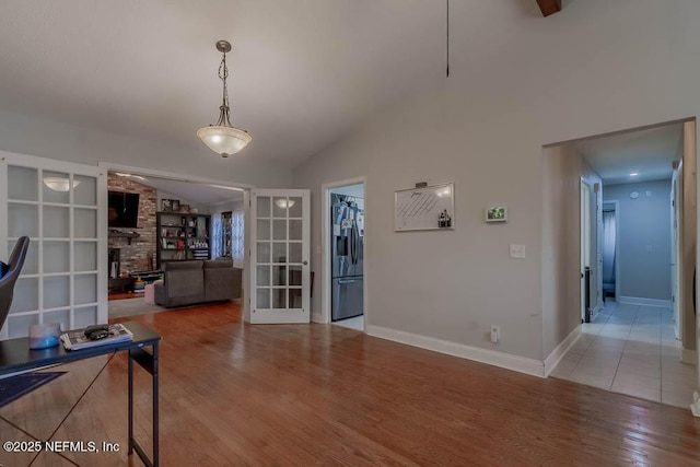 interior space featuring light hardwood / wood-style floors, french doors, a stone fireplace, and high vaulted ceiling