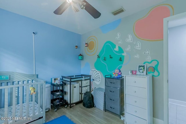 bedroom featuring ceiling fan, light wood-type flooring, and a crib