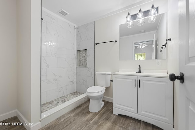 bathroom featuring toilet, vanity, ceiling fan, and a tile shower