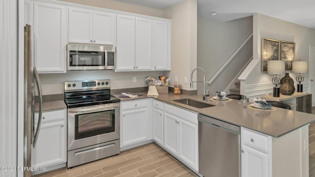 kitchen with kitchen peninsula, sink, stainless steel appliances, and white cabinetry