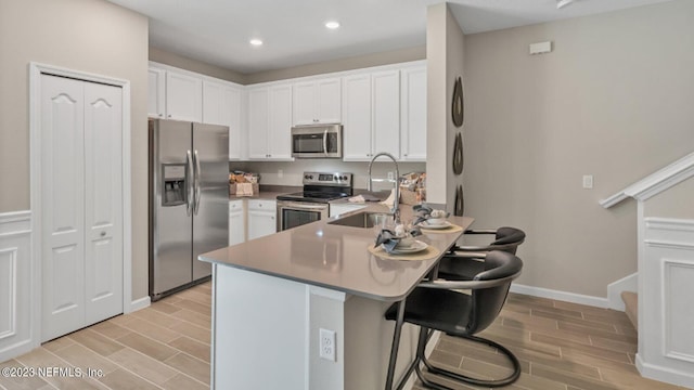 kitchen featuring kitchen peninsula, stainless steel appliances, white cabinetry, and a breakfast bar