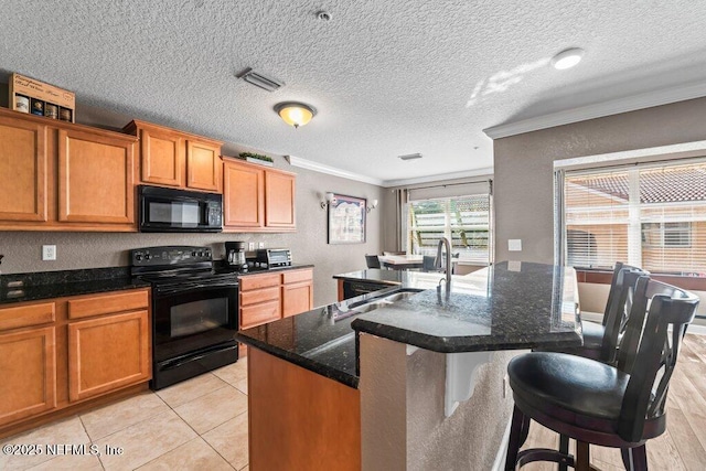 kitchen featuring an island with sink, dark stone countertops, a textured ceiling, crown molding, and black appliances