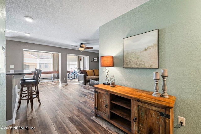 interior space featuring ceiling fan, wood-type flooring, a textured ceiling, and ornamental molding