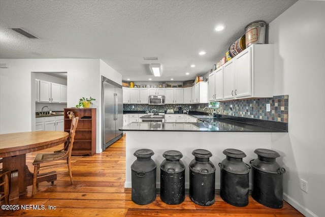 kitchen with light hardwood / wood-style floors, kitchen peninsula, sink, white cabinetry, and appliances with stainless steel finishes